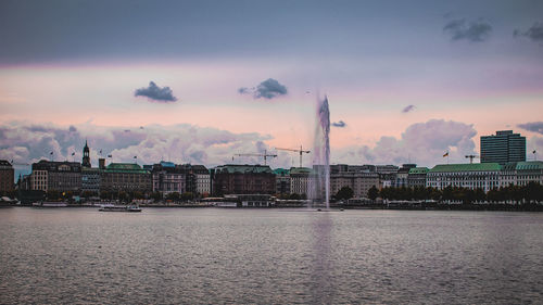 City by river against sky during sunset