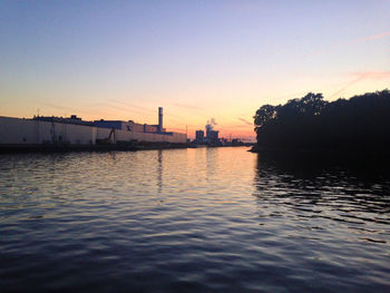 View of calm river with buildings in background at sunset