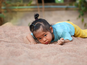 Portrait of cute girl lying on sand at playground