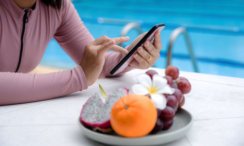 Midsection of woman holding mobile phone while swimming in pool