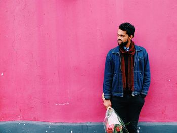 Young man with flower bouquet standing against pink wall