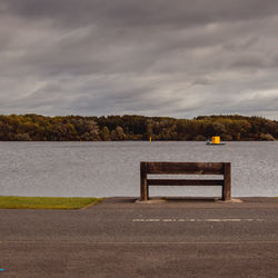 Empty bench by lake against sky