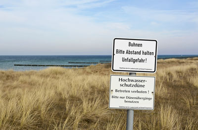 Information sign on beach against sky