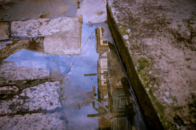 Reflection of built structure in puddle against sky