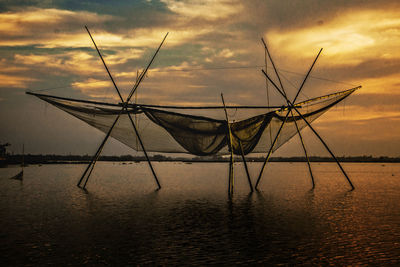 Fishing net on sea against sky during sunset