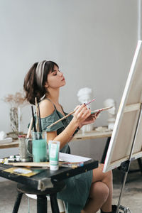 Young woman painting on canvas while sitting on table