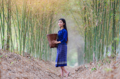 Young woman wearing traditional clothing while holding basket in bamboo grove