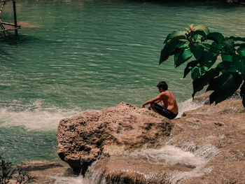 Rear view of  man sitting on rock by sea