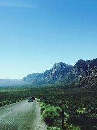 Country road leading towards mountains against blue sky