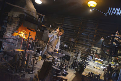 The blacksmith manually forging the red-hot metal on the anvil in smithy with spark fireworks