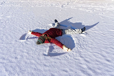 Young woman lying in the fresh snow and making a snow angel. winter walking and fun concept, holiday
