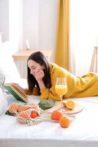 Young woman reading book while lying on bed at home