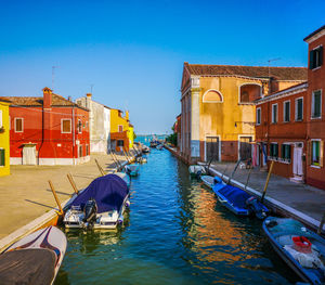 Boats moored in canal amidst buildings against clear blue sky