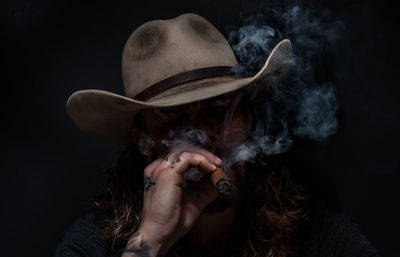 Portrait of young man holding hat against black background