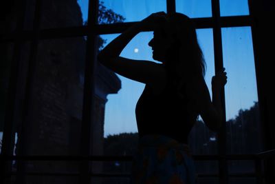 Rear view of silhouette woman standing in window