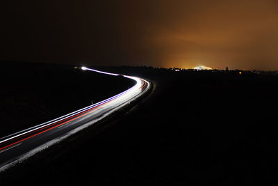 Light trails on road against sky at night