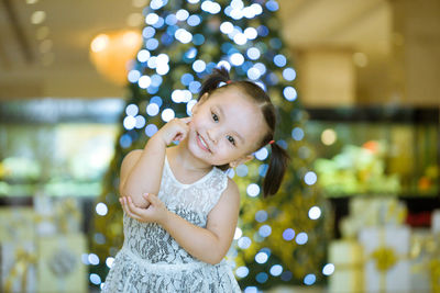 Portrait of cute girl standing against illuminated christmas tree