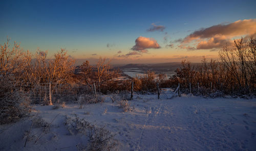 Snow covered field against sky during sunset