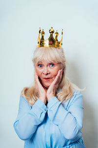 Portrait of smiling senior woman with crown against wall