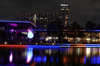 Illuminated city by river against sky at night