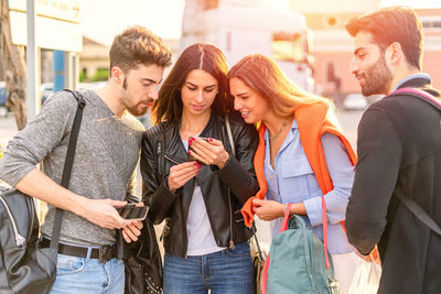 Friends looking at mobile phone while standing in city