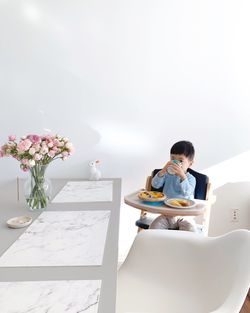 Portrait of boy having breakfast against white wall at home