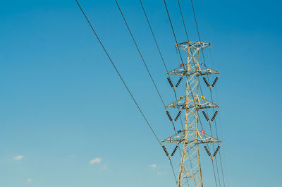 Low angle view of electricity pylon against blue sky