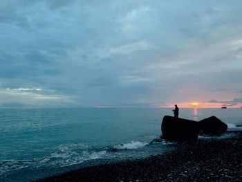 Silhouette person in sea against sky during sunset