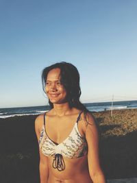 Portrait of beautiful woman standing at beach against clear sky