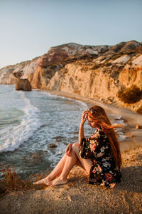 Young woman on rock at beach against sky