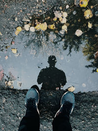 Low section of man standing by autumn leaves in lake