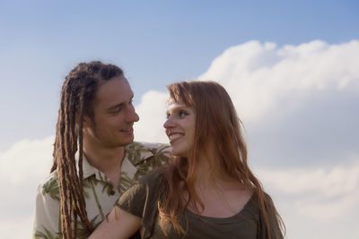 Smiling young couple looking at each other against sky