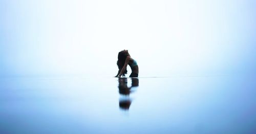 Side view of young woman standing in calm lake against clear sky