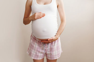 Midsection of pregnant woman standing against wall