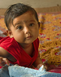 Cute indian baby lying on bed sheet over a mat looking at the camera.