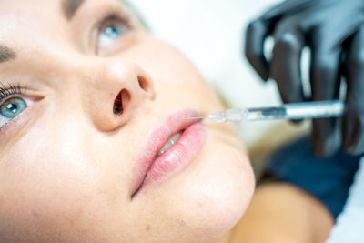 Cropped hand of cosmetician injecting fillers in woman lips