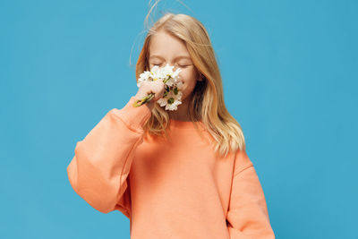 Cute girl smelling flowers while standing against blue background