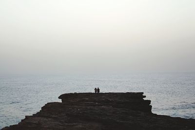 People standing on rock by sea against sky