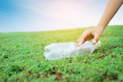 Cropped hand holding plastic bottle on grassy field against sky