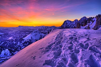 Scenic view of snow covered land and mountains against sky during sunset