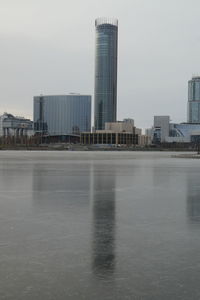 Modern buildings by river against sky in city
