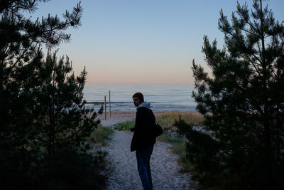 Man standing on shore against sky during sunset