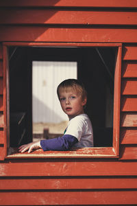 Side view portrait of cute boy seen through window in house