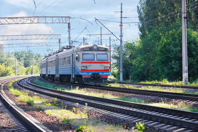 An old train rushes along the railway leaving the city on a summer sunny day.