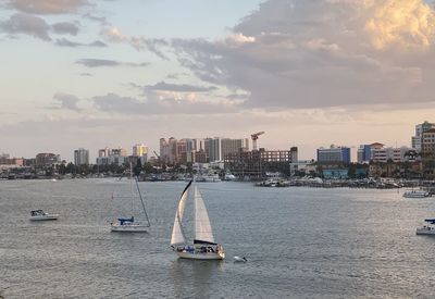 Sailboats in sea by buildings against sky