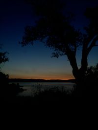 Silhouette trees by lake against sky at sunset