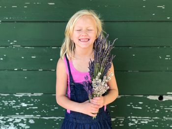 Cute girl holding flowers while standing against wooden wall