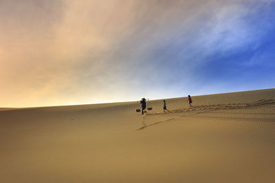 People on sand dune in desert against sky