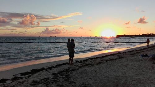 Woman standing on beach against sky during sunset