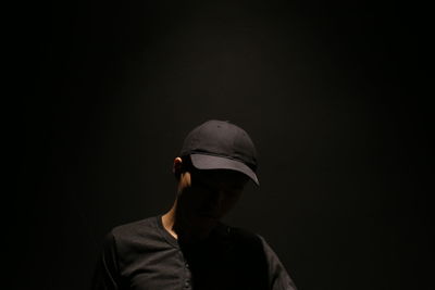Man wearing cap standing against black background